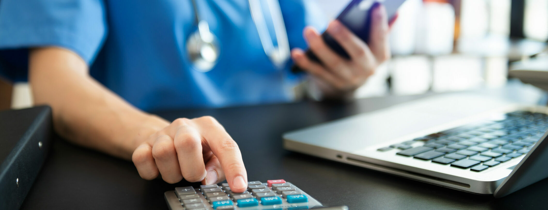 Hand of a doctor using a calculator, smartphone, and computer for medical costs in hospital